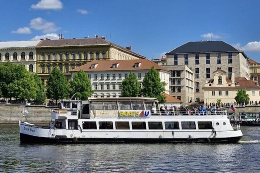 A white riverboat with "BOATS" written on its side, docked near a city with historic buildings and trees along the riverbank. 4