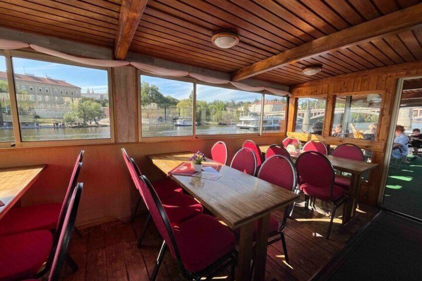 A restaurant with wooden ceiling and red chairs, overlooking a river. 4