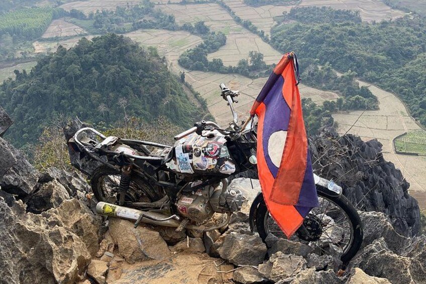 A motorcycle parked on a rocky mountain edge with a flag. 3