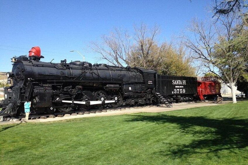Eine schwarze Dampflokomotive mit der Nummer 3759, beschriftet mit 'Santa Fe', steht auf einem Gleis mit Gras und Bäumen im Hintergrund. 4