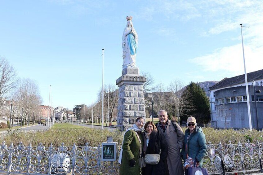 Un gruppo di persone in piedi di fronte a una statua in un parco, con recinzioni metalliche e edifici sullo sfondo. 3