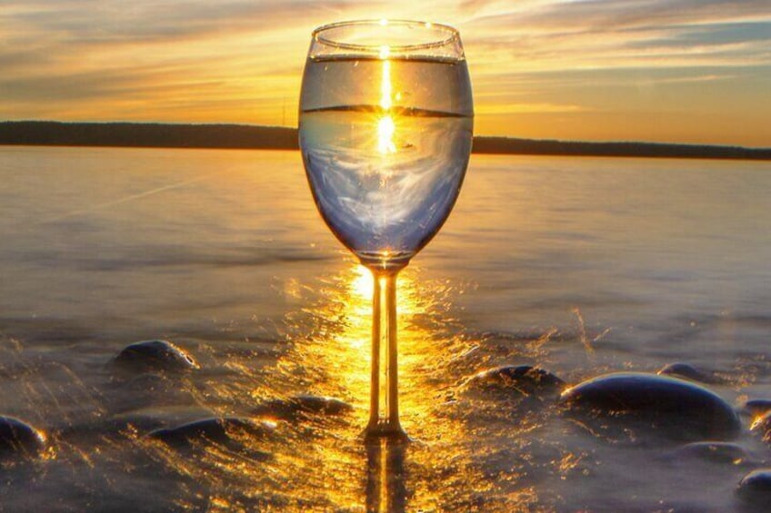 Un verre d’eau posé sur une surface réfléchissante, avec un coucher de soleil en arrière-plan. 1