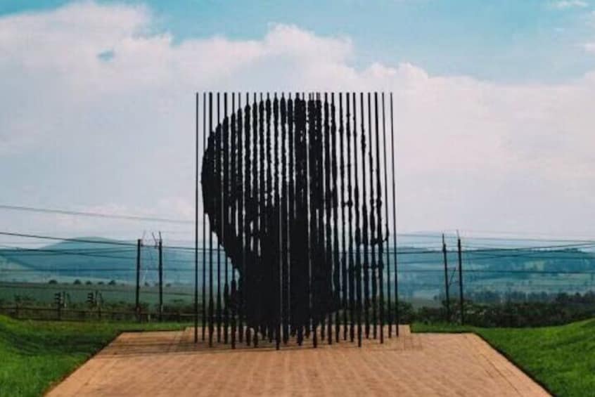 A large silhouette of a person's head and shoulders made of vertical poles, set against a rural landscape with fields and power lines. 5