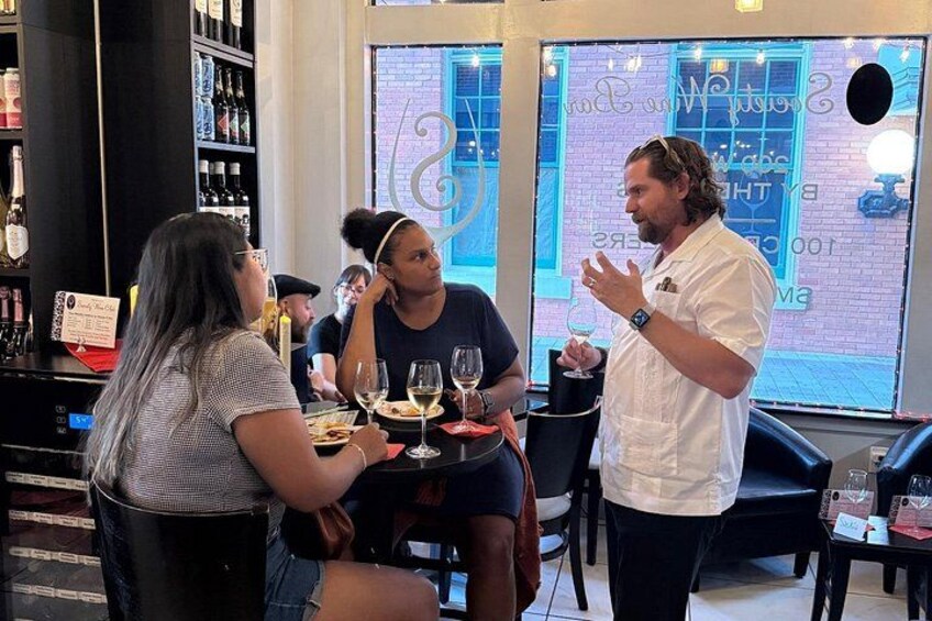 En bardisk med gæster ved bordene, en bartender stående, og en menutavle i baggrunden. 3