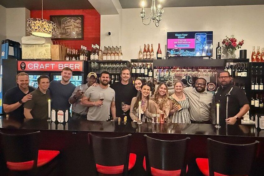 En gruppe mennesker i en bar med et skilt der viser 'CRAFT BEER', diverse flasker og et tv-skærm. 5