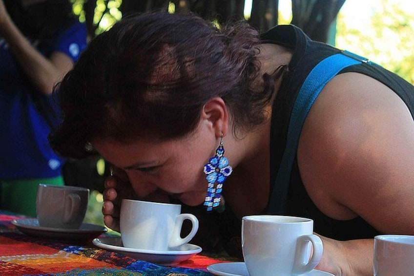 A person drinking from a white cup at a table with a colorful tablecloth. 2