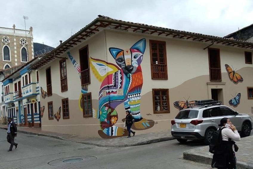 A street with colorful murals, a building with a clock tower, and a parked car. 3