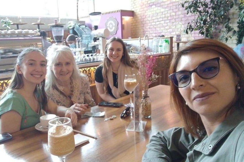 A group of people sitting at a wooden table in a cafe with a brick wall and a window in the background. 1