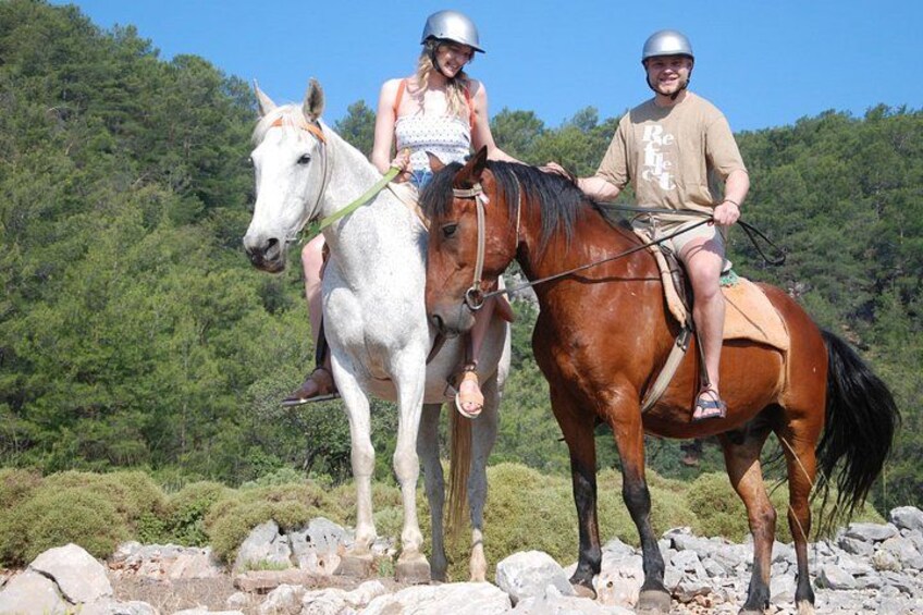 Deux personnes à cheval sur un sentier rocailleux, avec une forêt en arrière-plan. 3