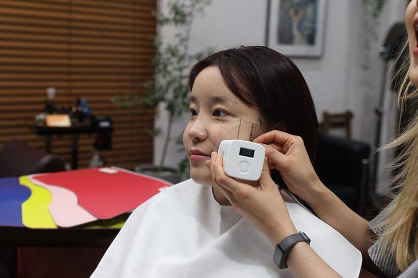 A person receiving a facial treatment with a device in a room with a table and a colorful mat. 3