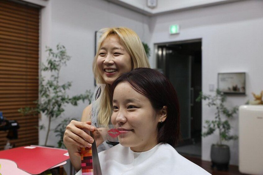 A person receiving a haircut in a salon with a mirror, a red chair, and a plant in the background. 2
