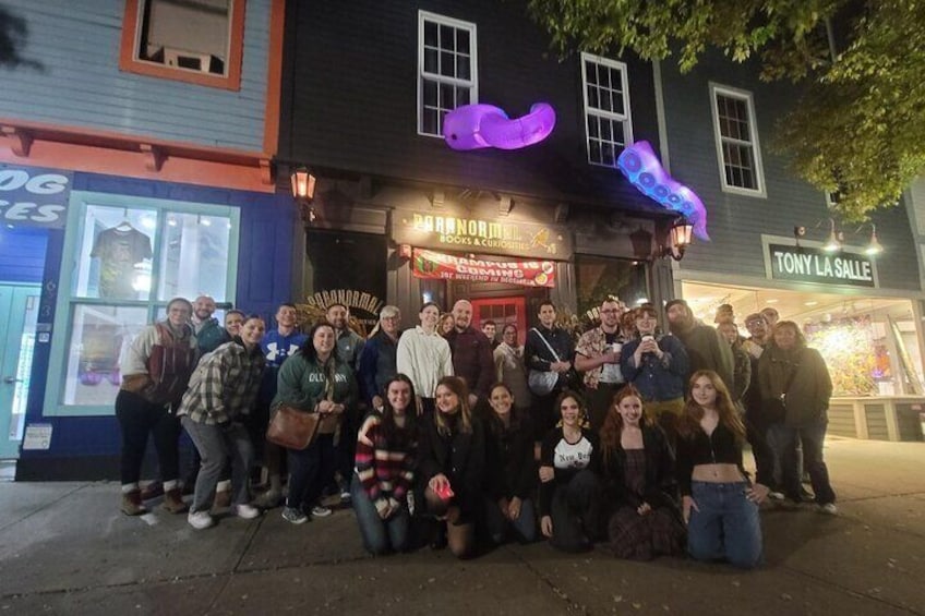 A group of people posing in front of a building with a neon sign. 1