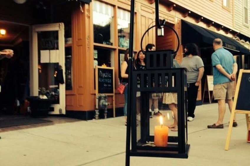 A street scene with a black lantern with a lit candle, a chalkboard sign, and people walking. 3