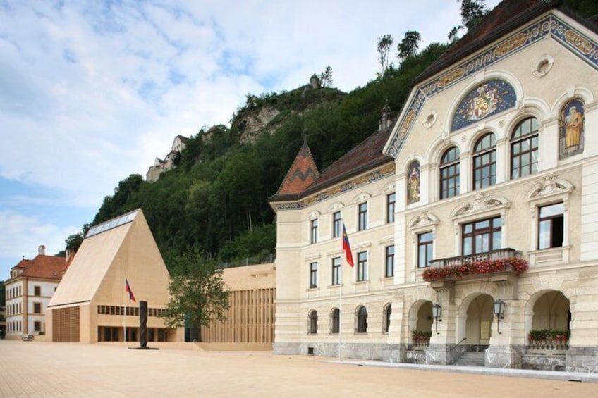 A historic building with classical architecture, a flag, and a mountainous backdrop. 5