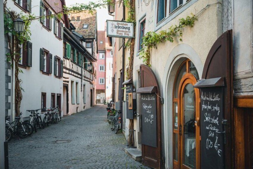 A cobblestone street lined with historic buildings, bicycles parked along the side, and chalkboard signs with writing. 2