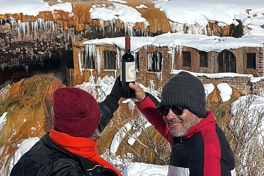 Two people taking a photo with a bottle in front of a cave with icicles. 5