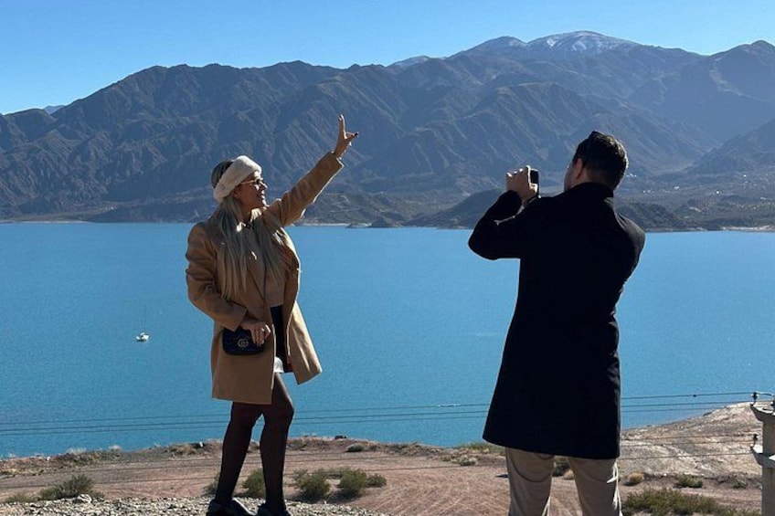 Two people taking photos of a lake with mountains in the background. 1