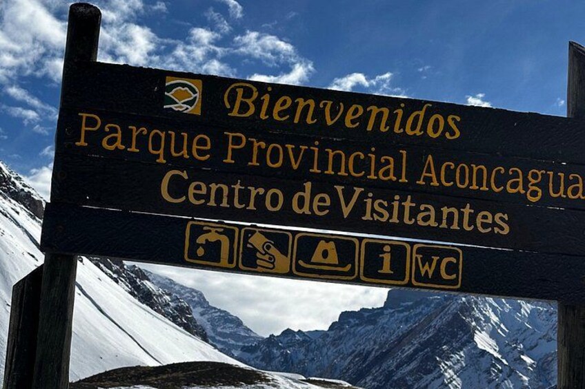 A sign with 'Bienvenidos Parque Provincial Aconcagua Centro de Visitantes' and symbols for facilities. 2