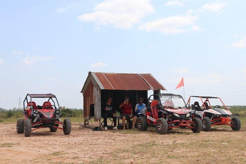 Three off-road vehicles parked in front of a small shed with people sitting inside. 3