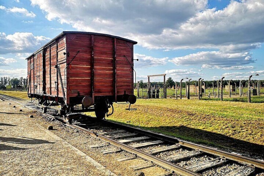 A red train car on tracks with a grassy field and a fence in the background. 1