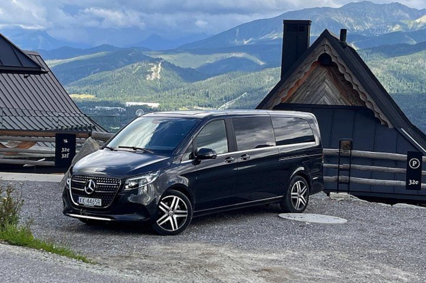 Een zwarte Mercedes-Benz Sprinter bestelwagen geparkeerd op een grindweg, met een bergachtig landschap op de achtergrond. 2