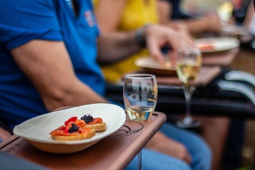A person in a blue shirt seated at a table with a plate of food and a glass of white wine. 4