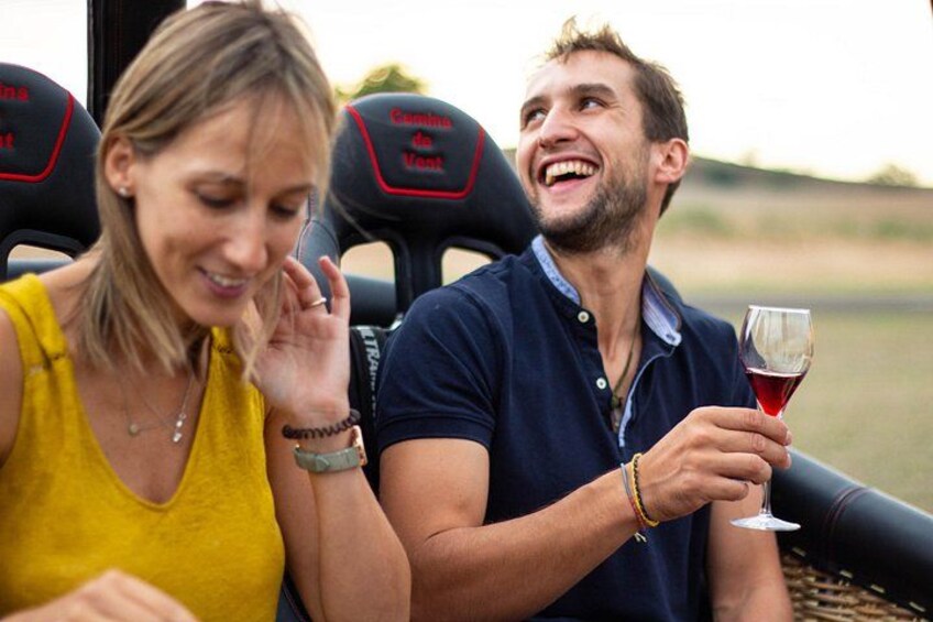 Two people sitting on a boat with a glass of red wine, a grassy landscape in the background. 5