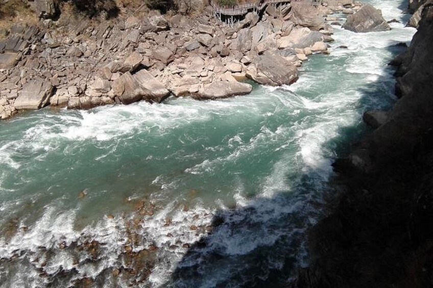 A river with white water rapids, rocky banks, and a bridge in the background. 4
