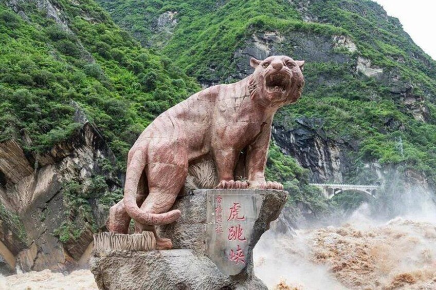 A stone lion statue on a cliff with a bridge in the background. 1