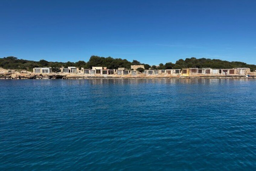 A coastal area with a row of buildings along the shore, a clear blue sky, and calm sea. 2