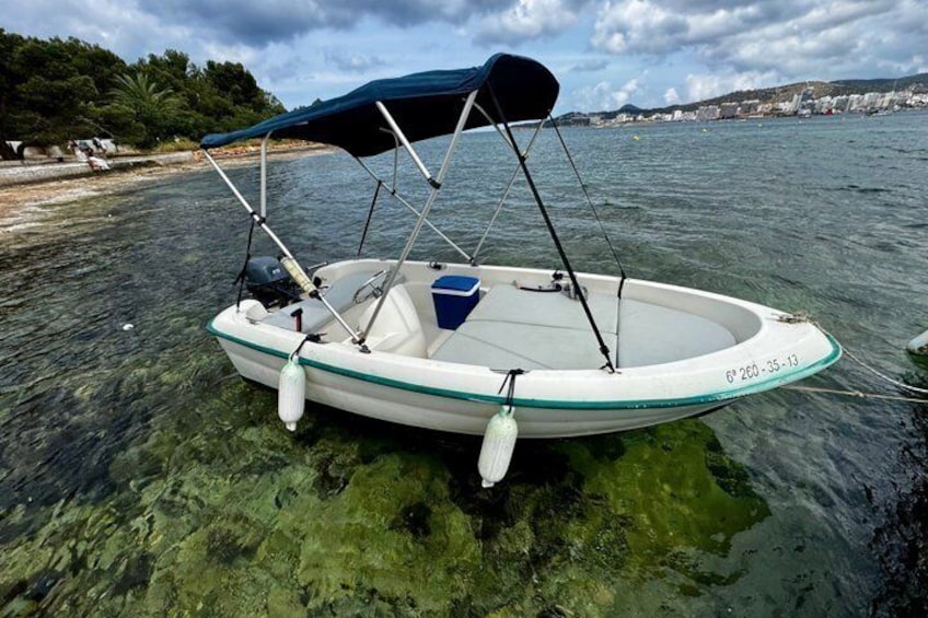 A small boat with a canopy, anchored near a beach with clear water and a distant shoreline. 1