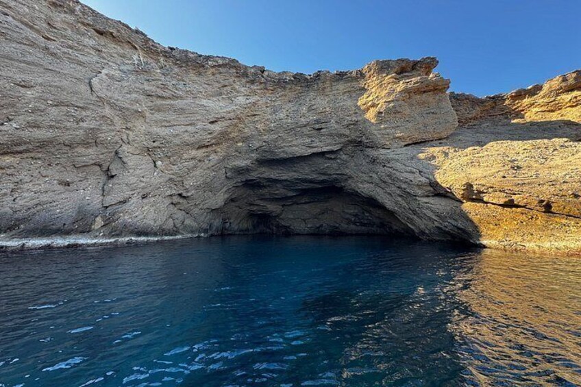 A rocky coastline with a cave entrance and clear blue water. 4