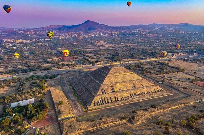 Een piramide met omliggende velden en luchtballonnen in de verte. 2