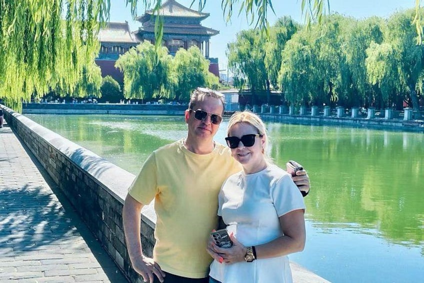 A couple standing by a calm water body with a traditional building in the background. 5