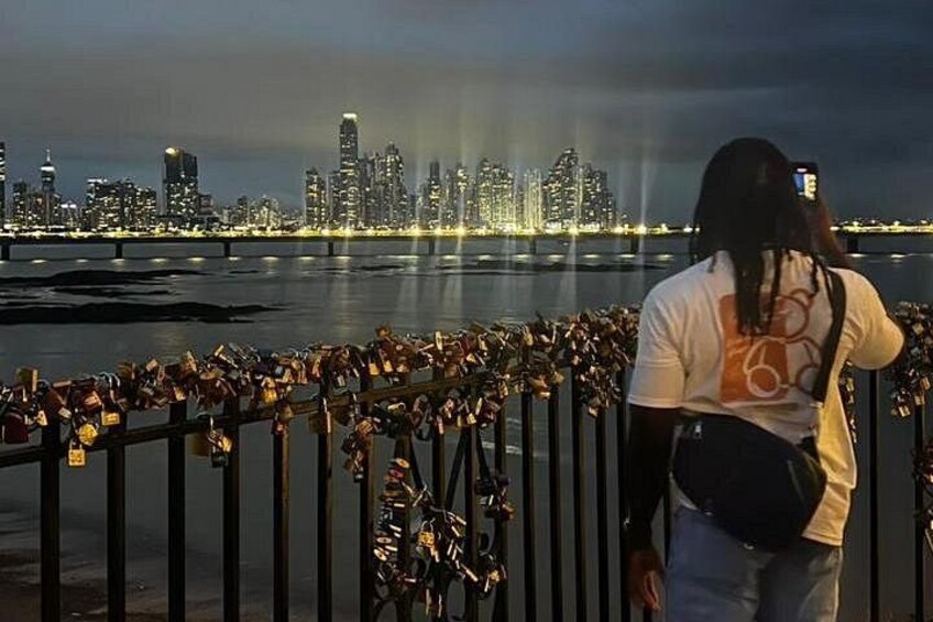 A person taking a photo of a city skyline at night with a bridge in the foreground. 2