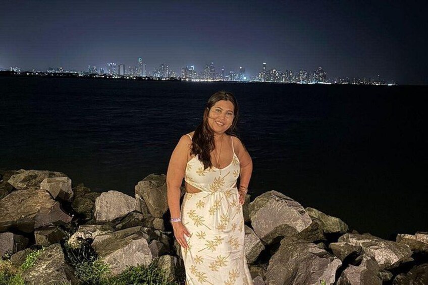 A person standing by a rocky shoreline with a city skyline in the background. 5