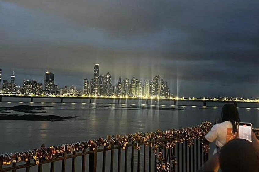 A city skyline at night with illuminated buildings across a body of water. 1