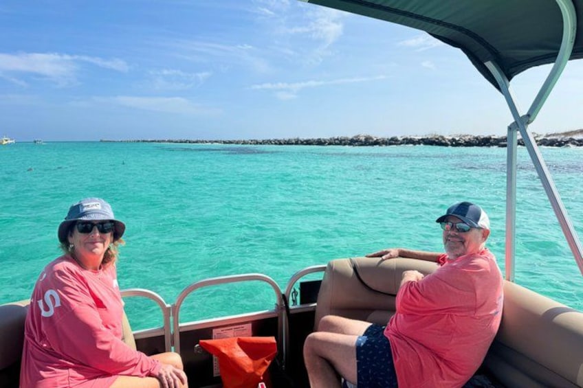 Twee personen op een boot, met turquoise water en een rotsachtige kustlijn op de achtergrond. 5