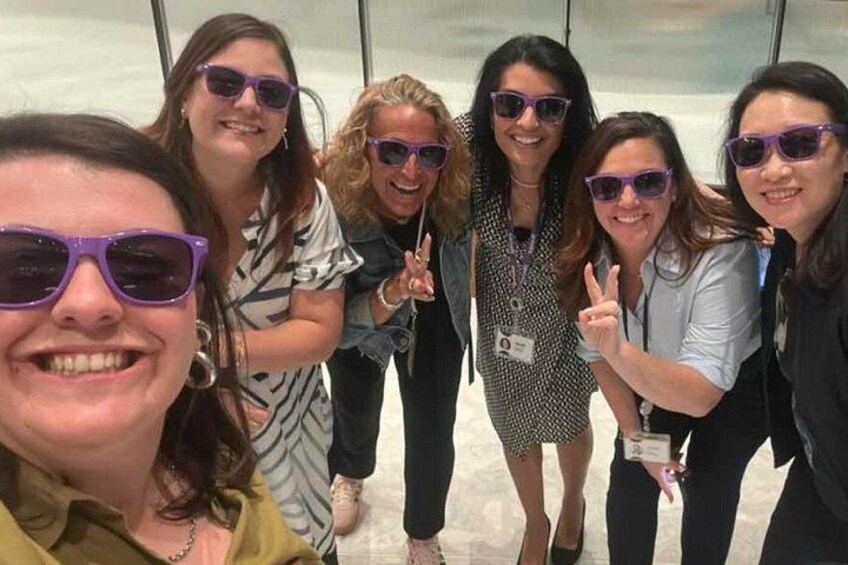A group of people posing for a photo in an indoor setting with a glass wall in the background. 2