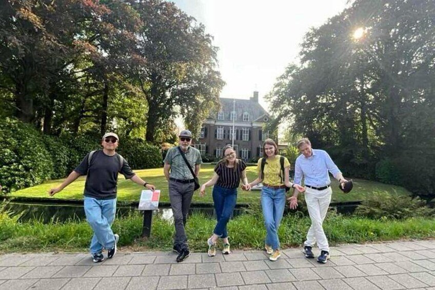 A group of people walking on a paved path in a park with trees and a building in the background. 5