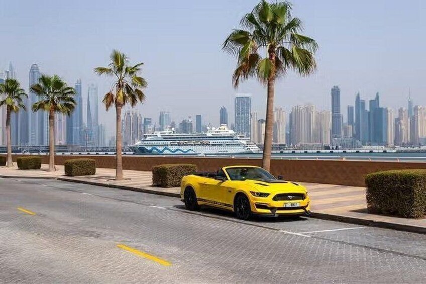 A yellow sports car parked on a road with palm trees and a cruise ship in the background. 3