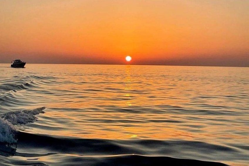 Een zonsondergang boven een rustige zee, met een boot in de verte. 5