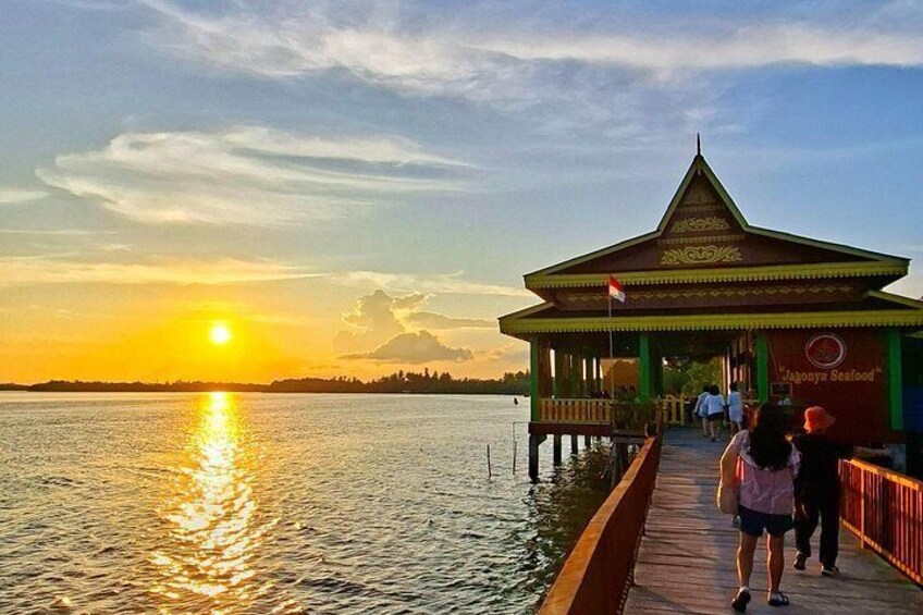 Un muelle se adentra en una masa de agua al atardecer, con un restaurante llamado 'Lagoona Seafood' a la derecha. 3