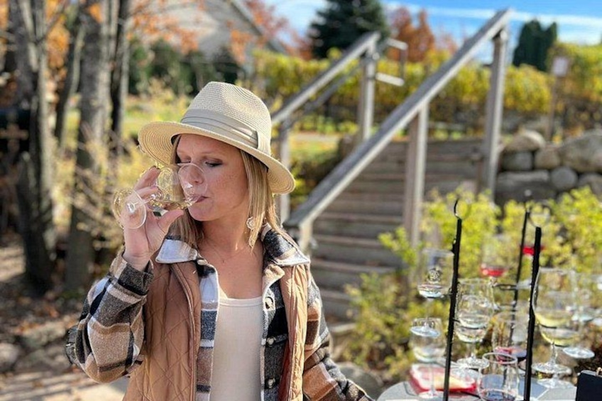 A person wearing a hat and a plaid shirt, holding a wine glass, with a table of wine glasses in the background. 2