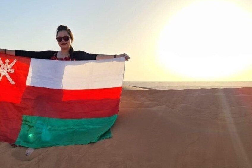A person holding a flag with horizontal stripes and a star emblem, standing on a desert with a clear sky. 3