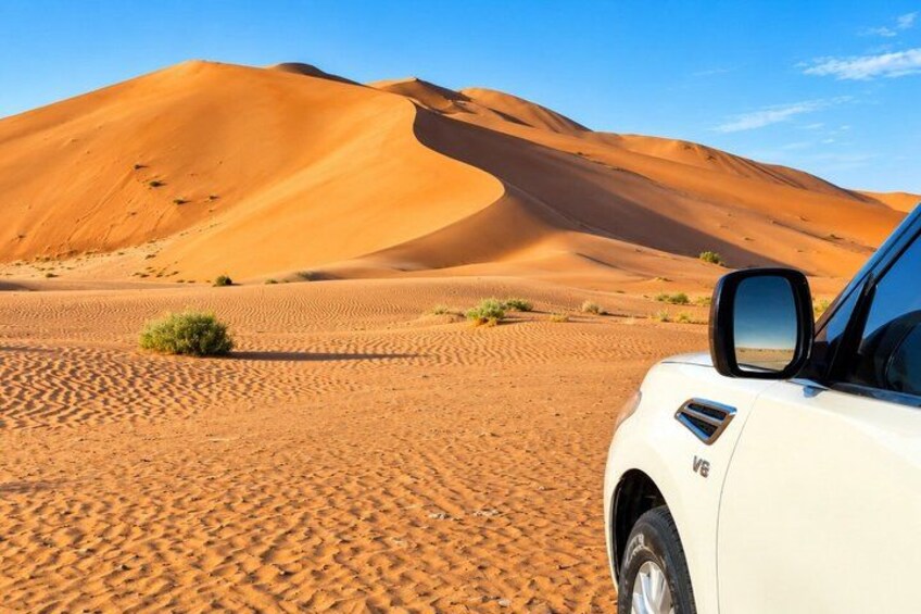 A white car parked in a desert with sand dunes in the background. 2