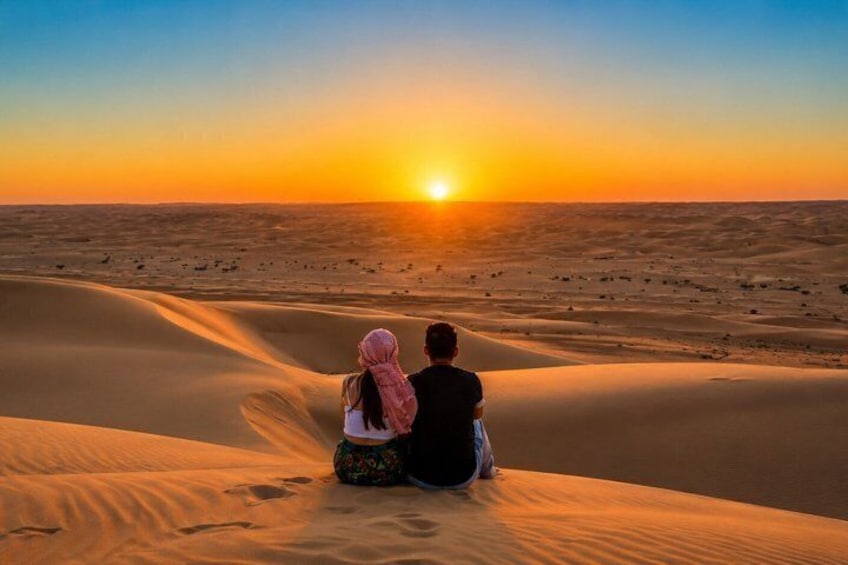 Two people sitting on sand dunes watching the sunset. 4