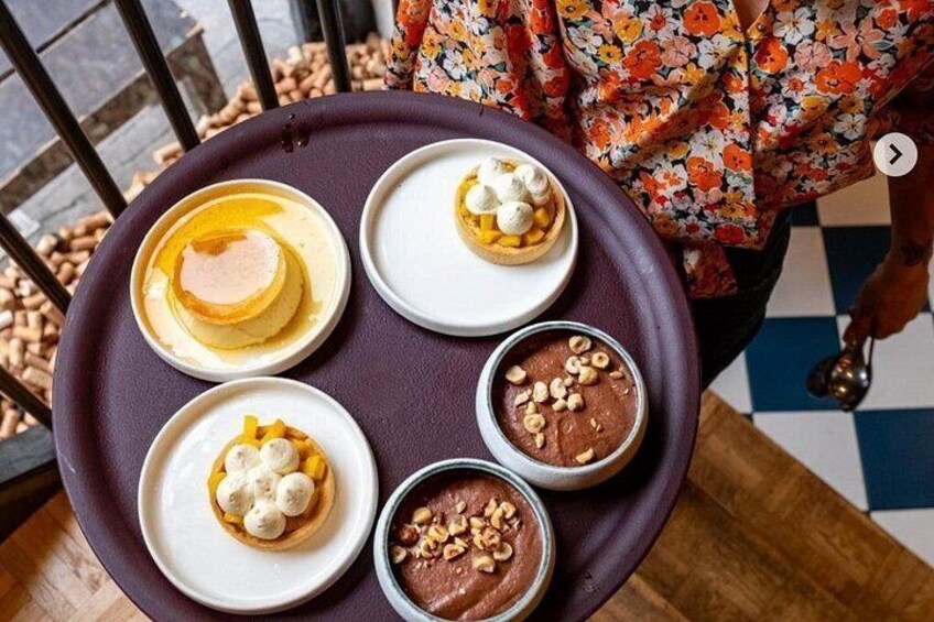 A tray with four dessert plates, including a flan, a dessert with whipped cream and fruit, a dessert with nuts, and a chocolate dessert. 5