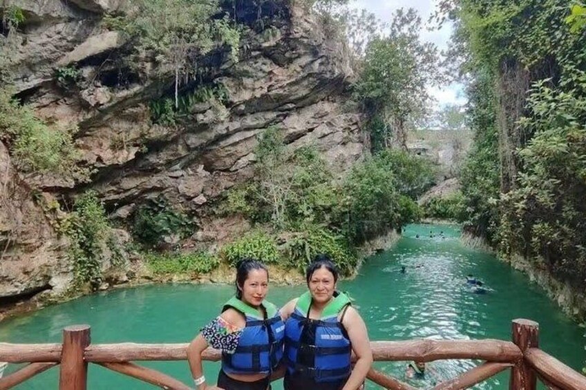 Two people wearing life jackets on a wooden bridge over a river with rocky cliffs and greenery. 5