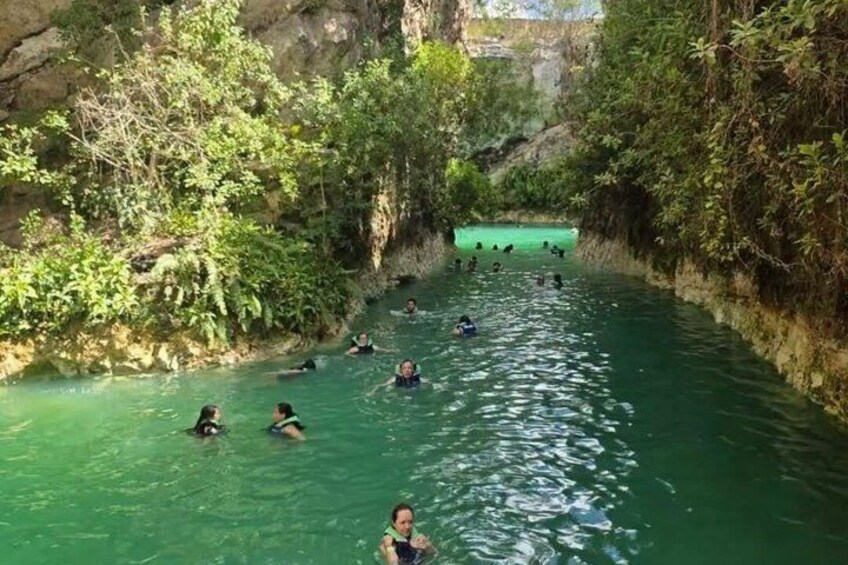 A group of people swimming in a narrow, greenish waterway surrounded by dense vegetation. 2